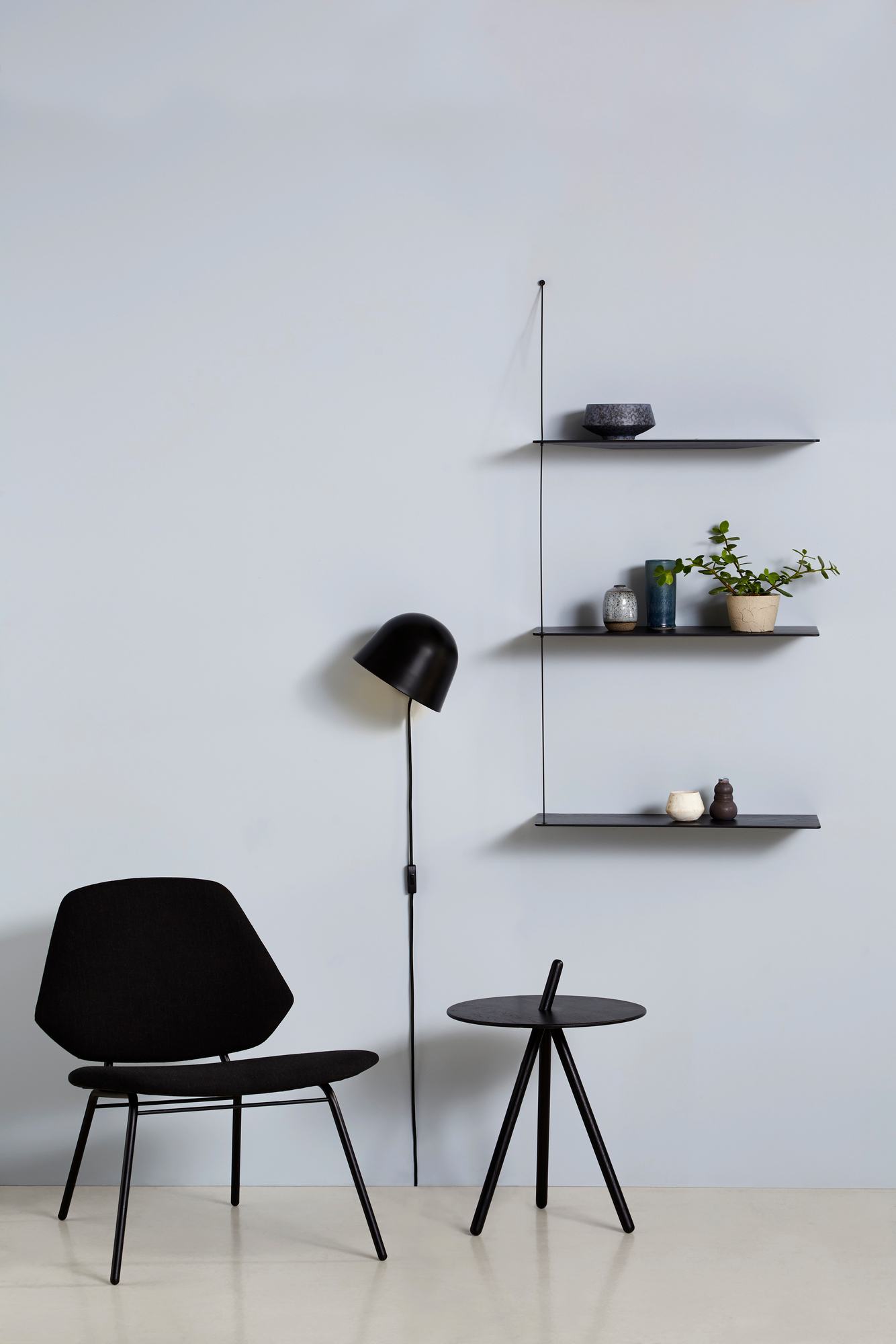 Kuppi Wandleuchte schwarz von Woud neben Stuhl und Regal mit Dekoration. Moderne Wandlampe.