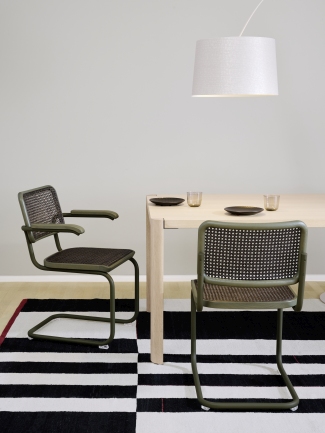 Zwei grüne Thonet S 64 V Freischwinger Stühle mit Rohrgeflecht an einem Esstisch auf einem Teppich.