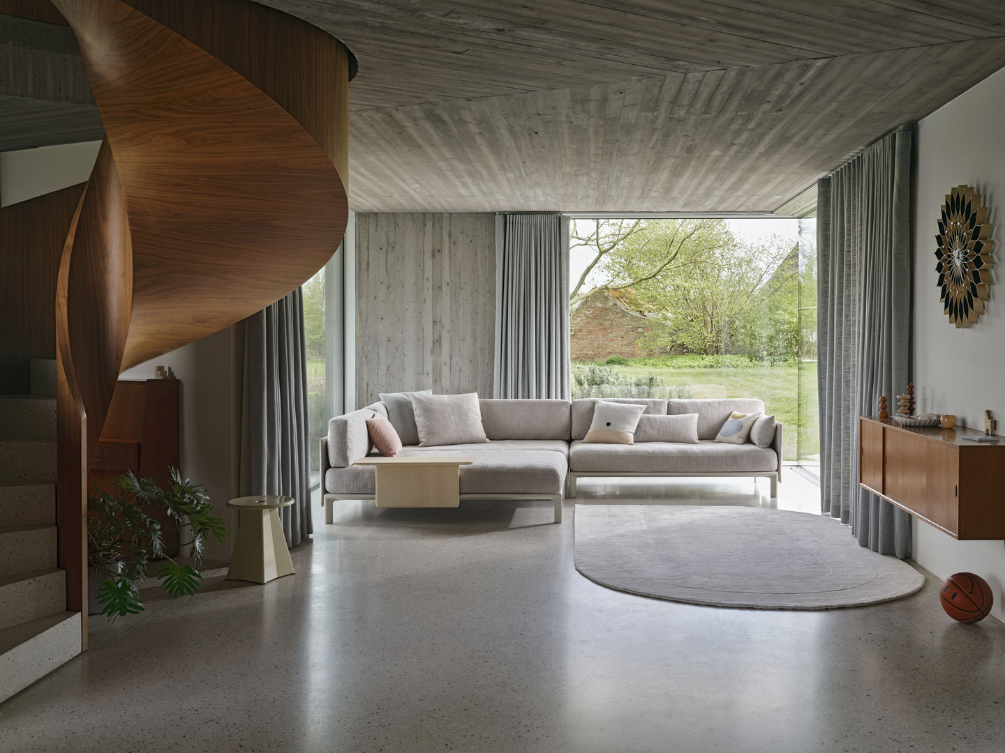 Helles Wohnzimmer mit großem Fenster und Anagram Rückenkissen/Seitenkissen von Vitra auf einem modernen Sofa.