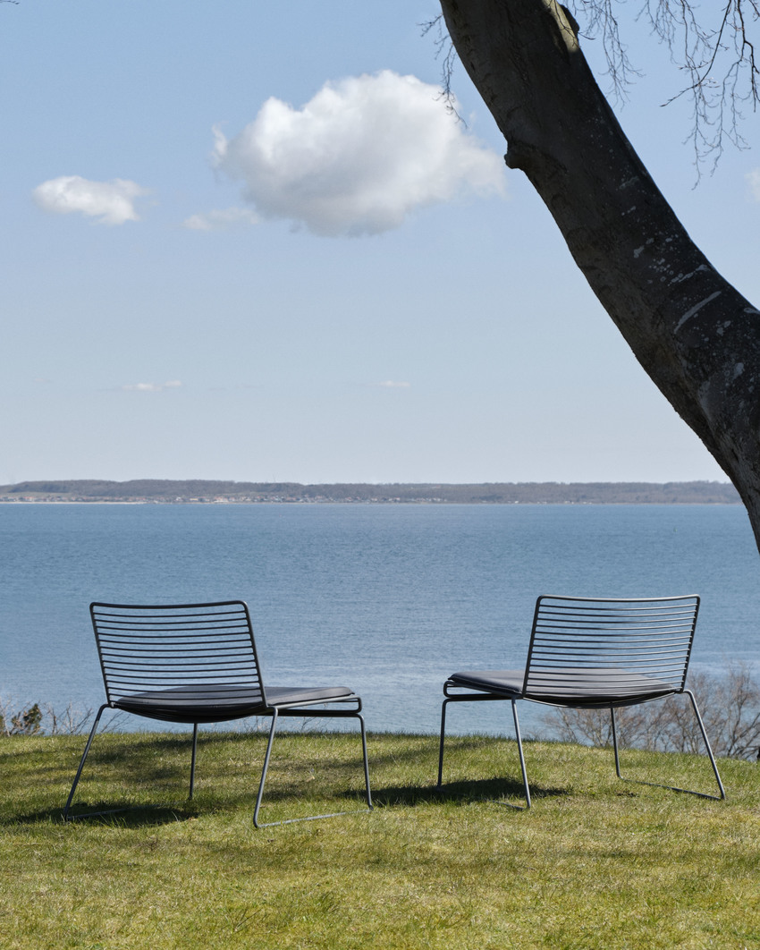 Zwei graue Hee Lounge Chairs von Hay auf einer Wiese mit Meerblick im Hintergrund.