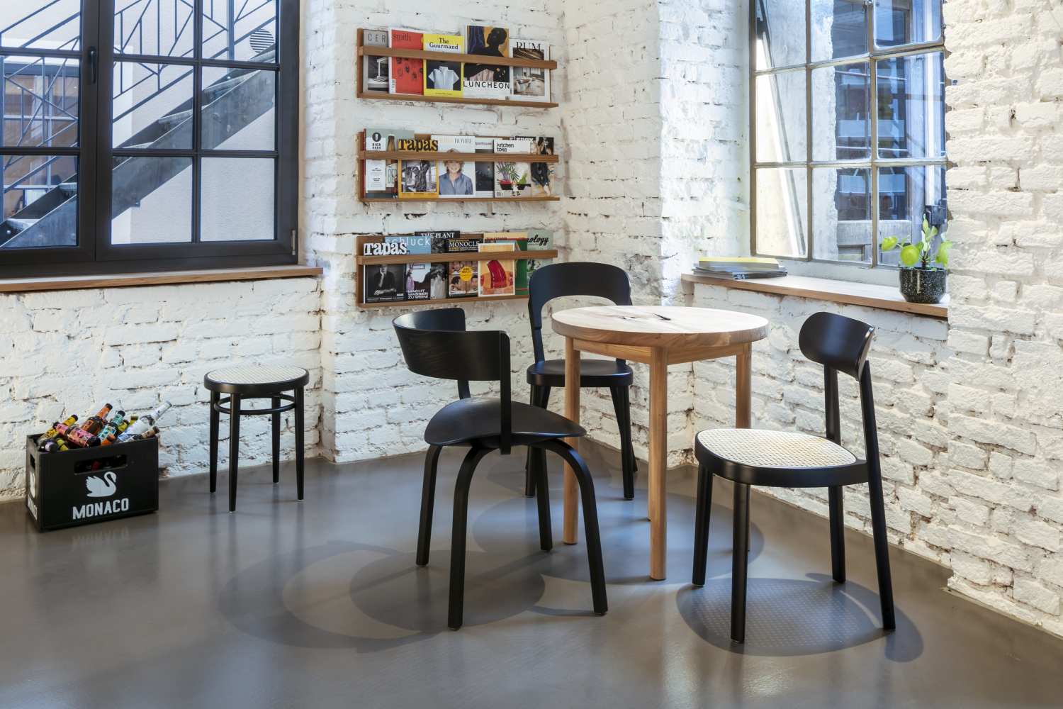 Esszimmer mit rundem Holztisch und schwarzen Holzstühlen mit Rattan-Sitzfläche vor weißer Backsteinwand.