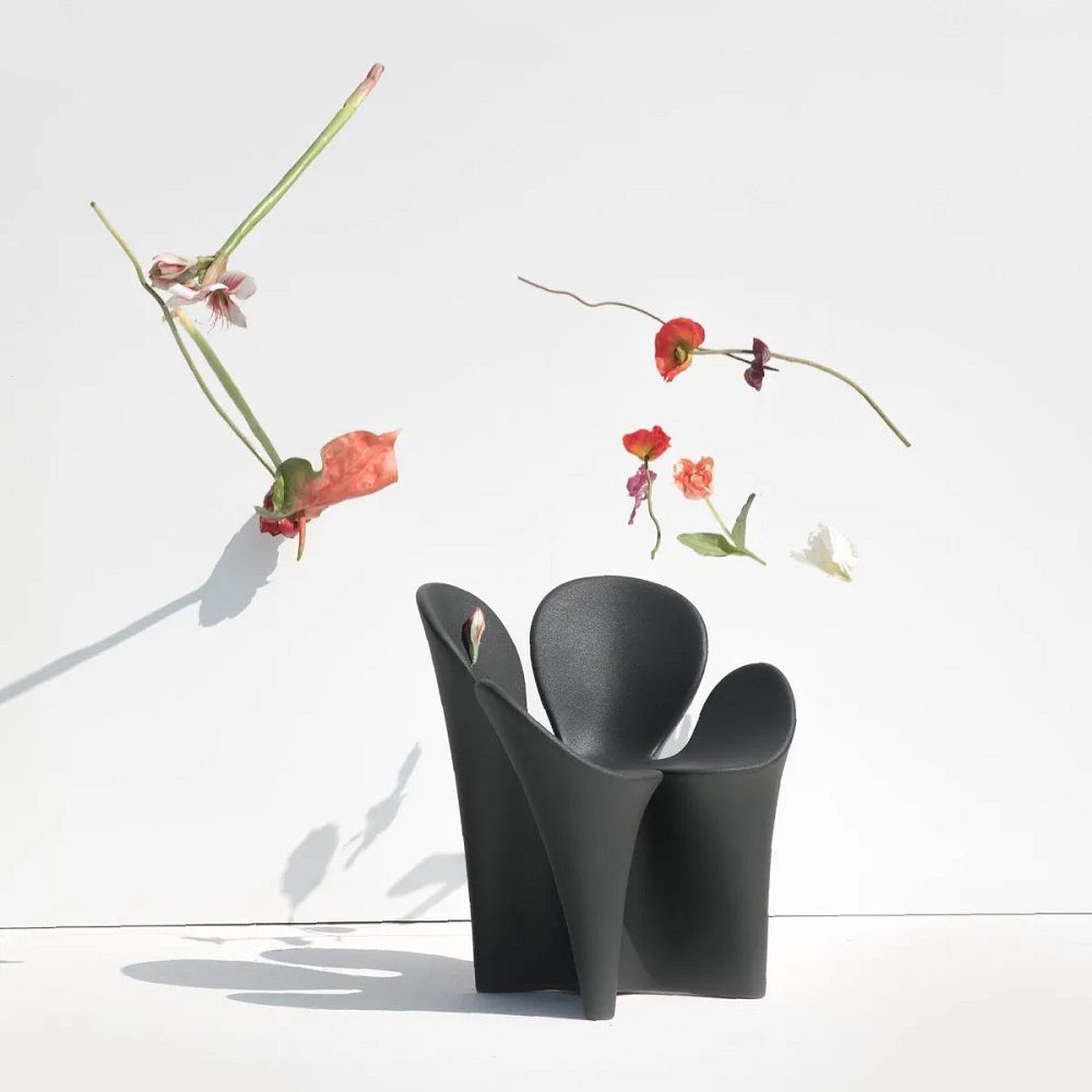 Schwarzer Clover Chair Armlehnstuhl von Driade mit Blumen vor weißem Hintergrund, modernes Möbeldesign.