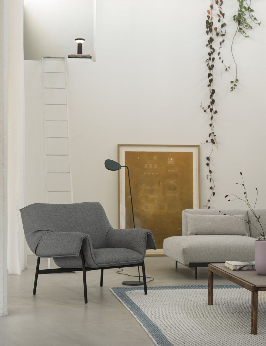 Grauer Sessel mit schwarzen Beinen in modernem Wohnzimmer mit Sofa, Teppich und Stehlampe.