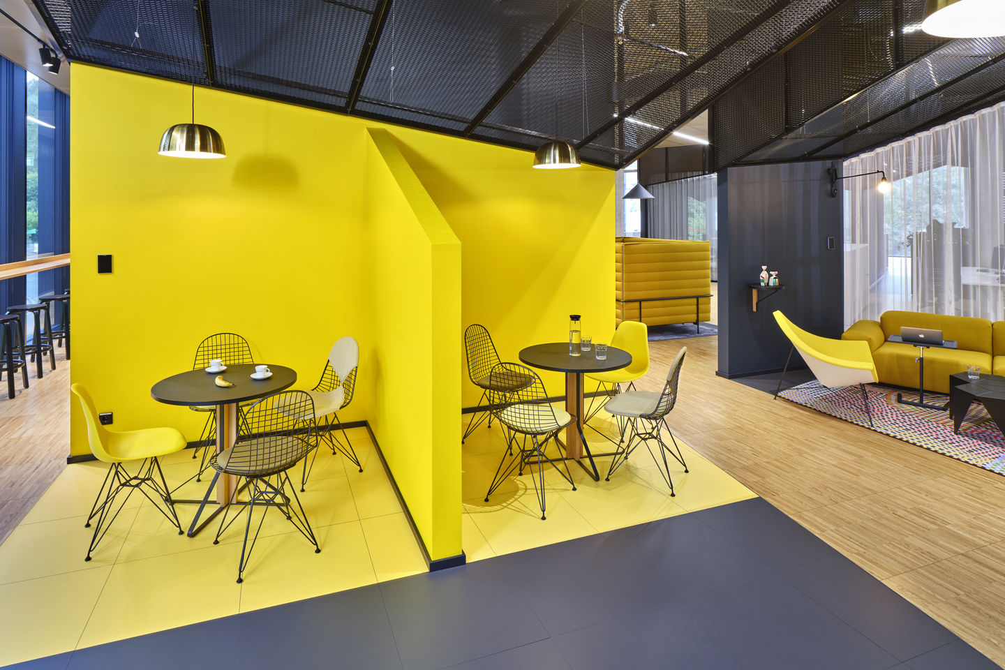 Innenaufnahme mit DKR Wire Chairs von Vitra, Sitz- und Rückenpolster, schwarze Drahtgestelle, gelbe Akzentwand.