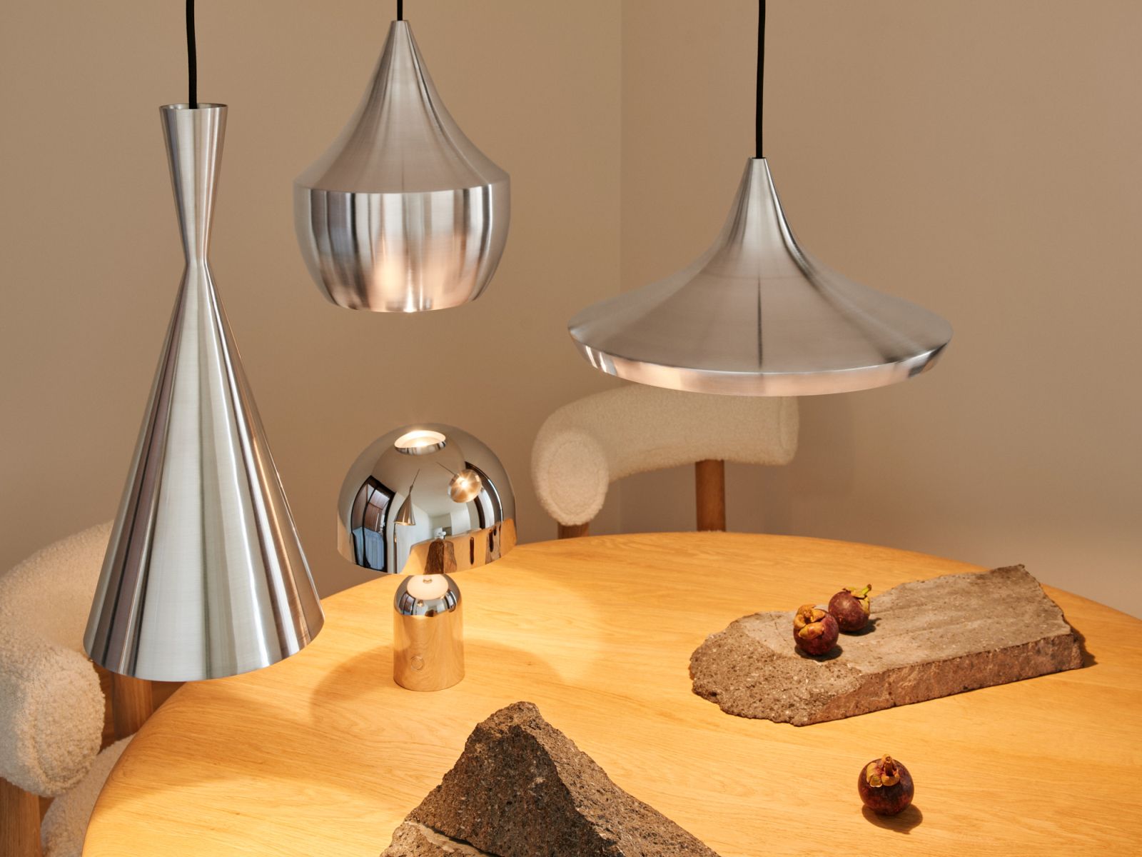 Nahaufnahme von Tom Dixon Unbeaten Pendelleuchten in verschiedenen Formen aus gebürstetem Edelstahl über einem Holztisch.
