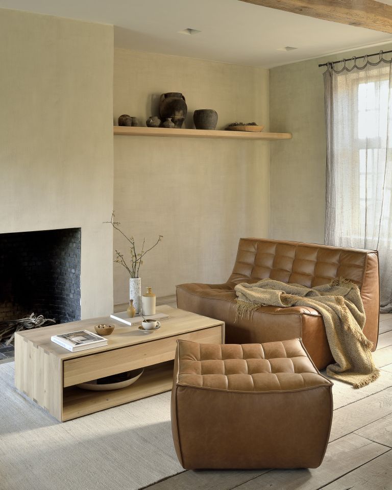 Wohnzimmer mit braunem Ledersofa, Hocker und Holztisch vor Kamin. Gemütliche Einrichtung für Wohnraum.