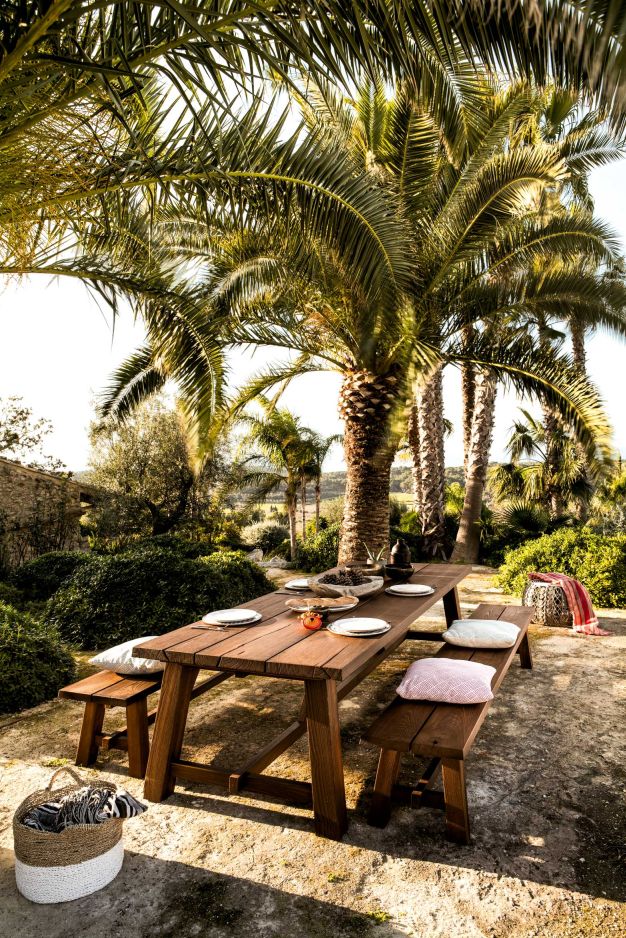 BC 08 Cantina Outdoor Sitzbank von Janua unter Palmen, rustikale Holzbank für Garten und Terrasse.