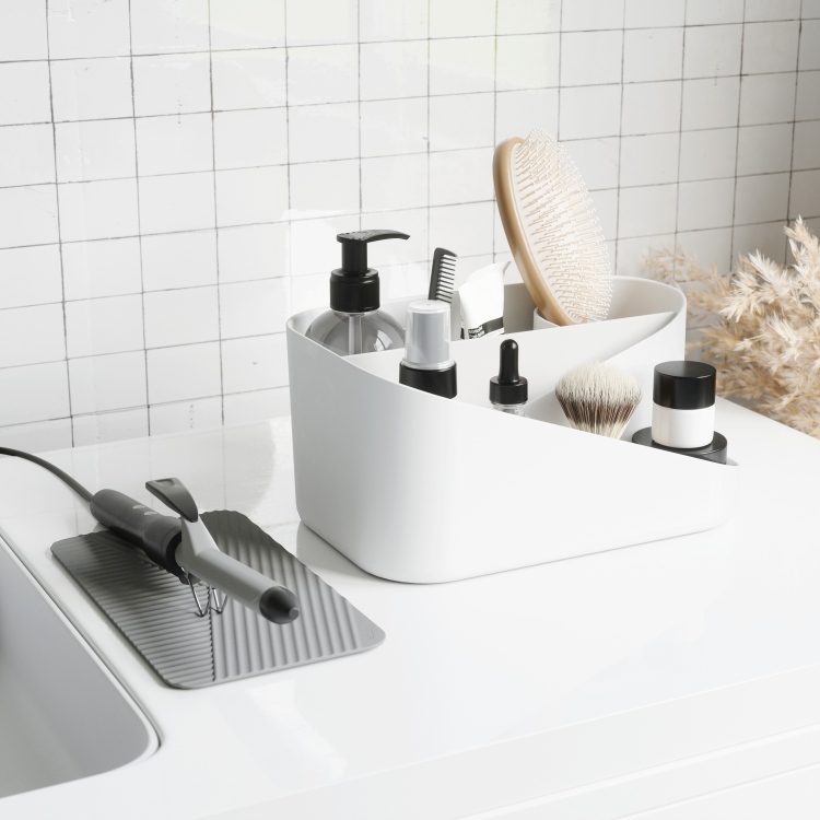 Weißer Glam Hair Organizer von Umbra mit Haarbürste, Kosmetikprodukten und Lockenstab auf weißer Oberfläche.