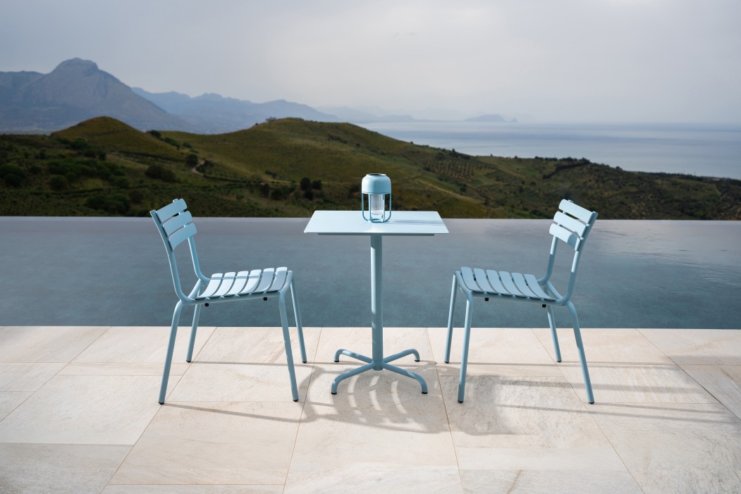 Zwei blaue Alua Dining Stühle von Houe und ein Tisch auf einer Terrasse mit Meerblick.
