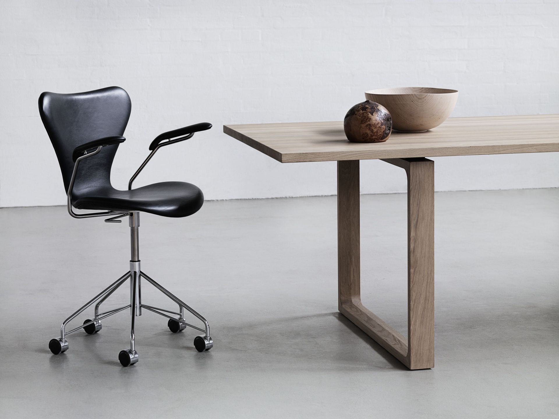 Schwarzer Bürostuhl mit Armlehnen und Holztisch mit Deko-Schale und Kugel für modernes Bürodesign.