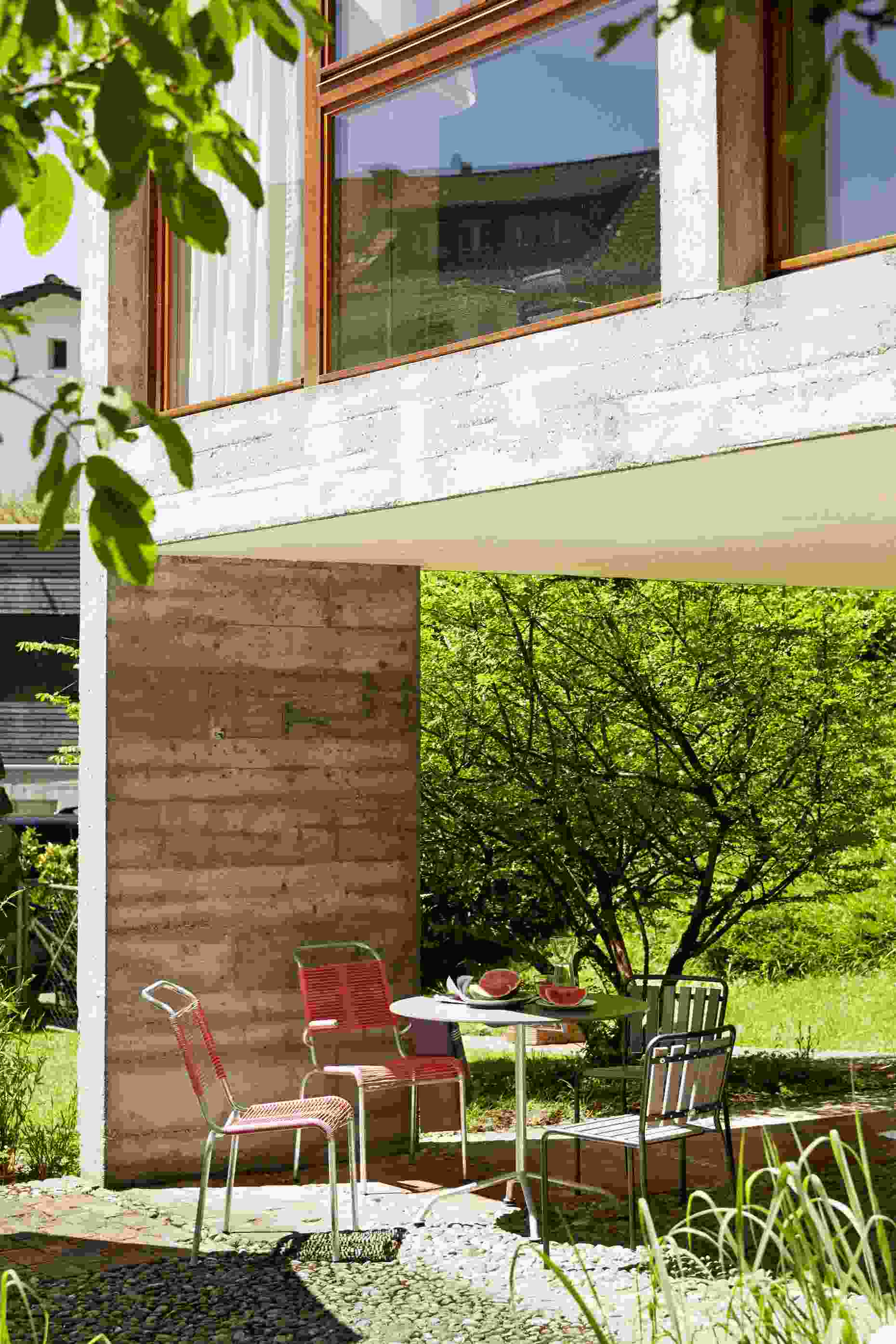 Haefeli Stuhl in Feuerrot auf Terrasse mit Tisch und Wassermelone im Garten. Outdoor Möbel.