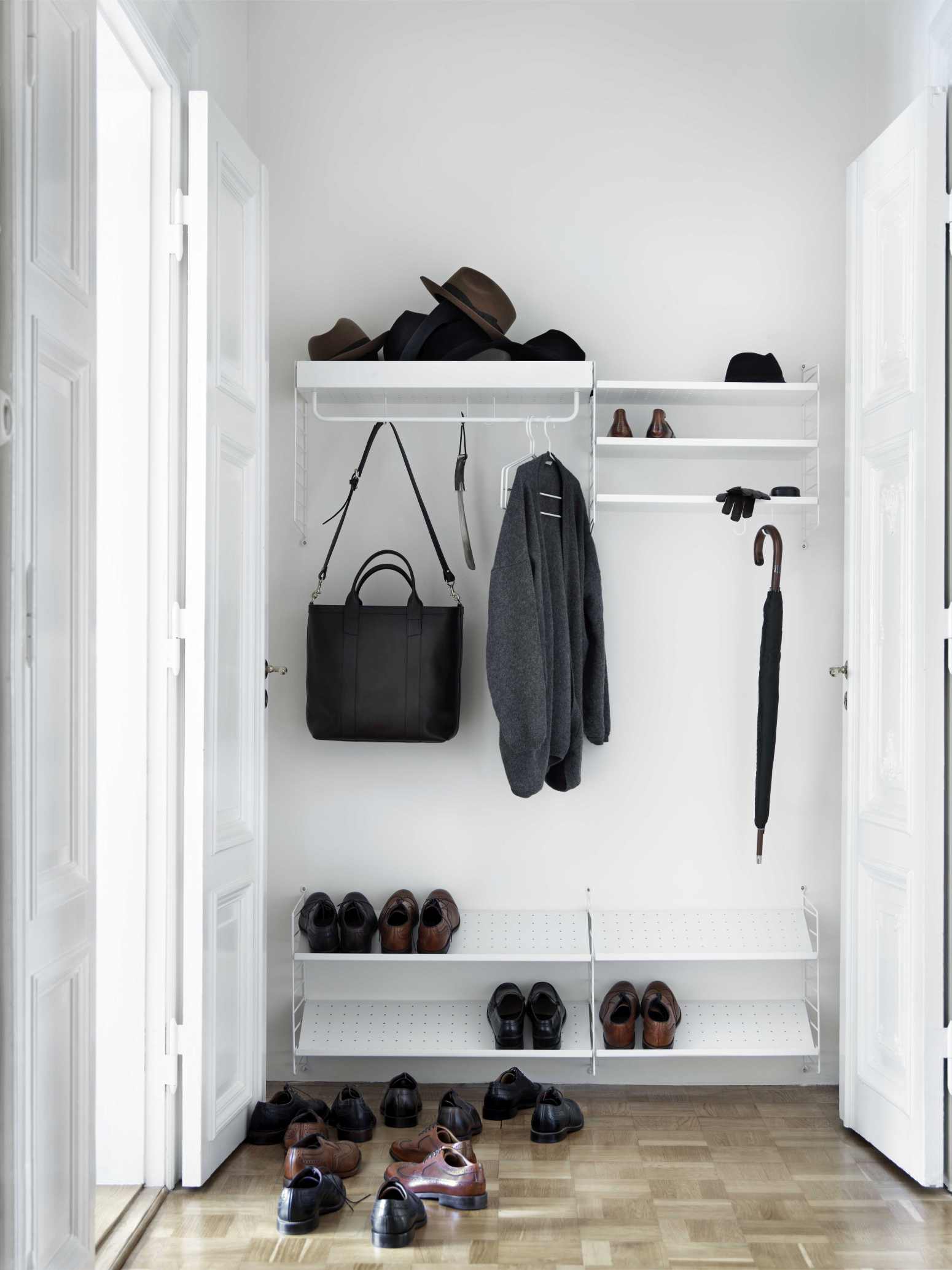 Weißes String Regalsystem im Flur mit Schuhen, Tasche, Jacke und Accessoires.