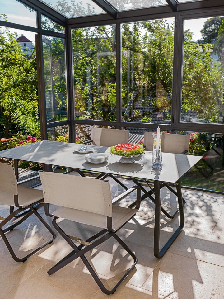 Ahoi Tisch Outdoor von Weishäupl mit Stühlen in Wintergarten, gedeckt mit Geschirr und Dekoration.