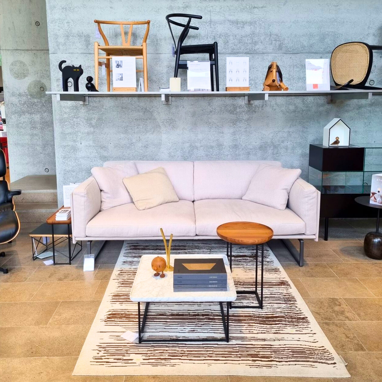 Helles Wohnzimmer mit modernem Sofa, Couchtisch und Teppich. Designermöbel und Accessoires auf einem Regal.