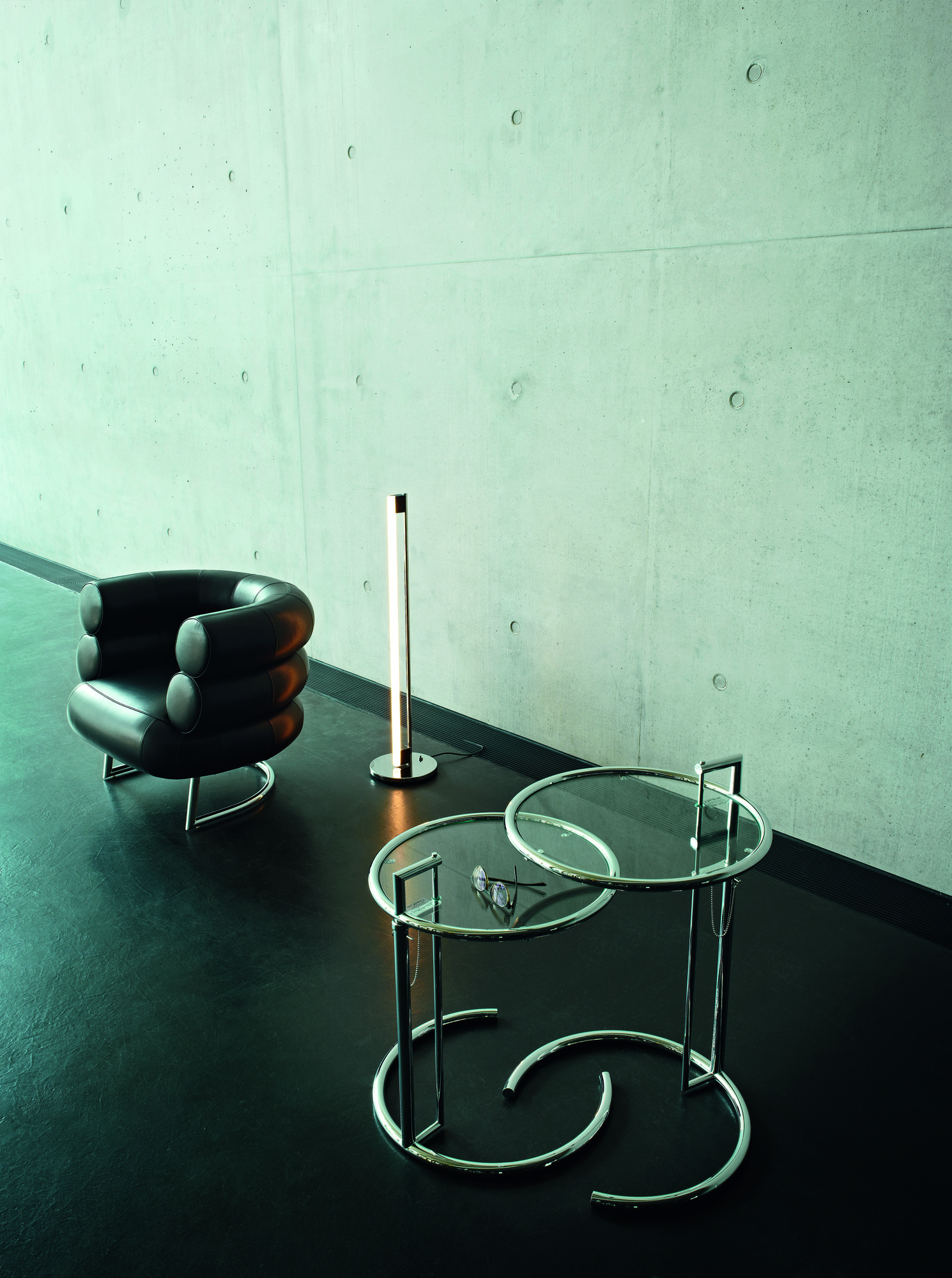 Moderner Adjustable Table E1027 Beistelltisch ClassiCon mit Glasplatte und verchromtem Gestell neben Sessel und Lampe.