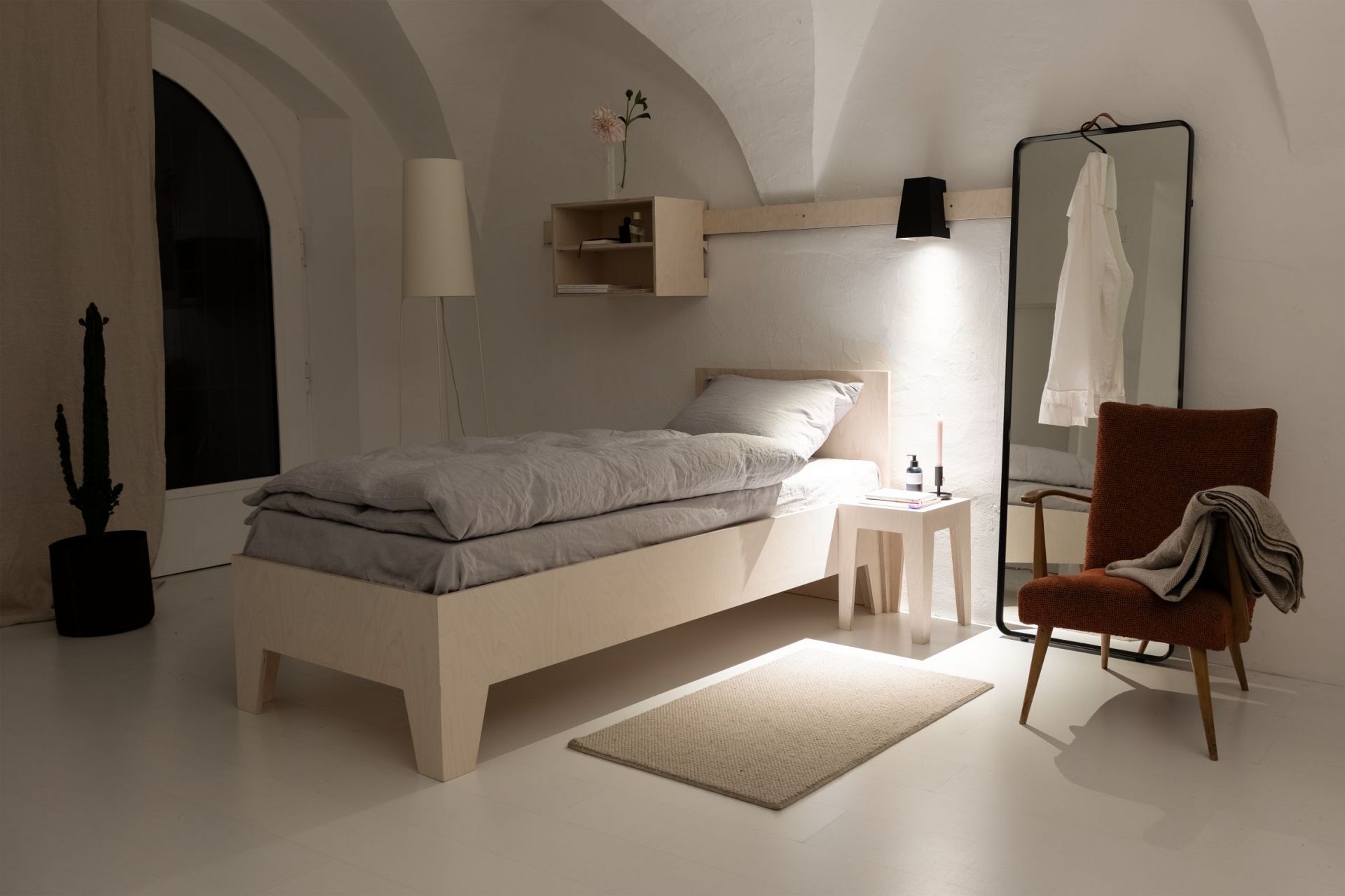 Schlafzimmer mit minimalistischem Holzbett, grauer Bettwäsche, Nachttisch, Spiegel und Sessel. Skandinavisches Design für Schlafzimmer.