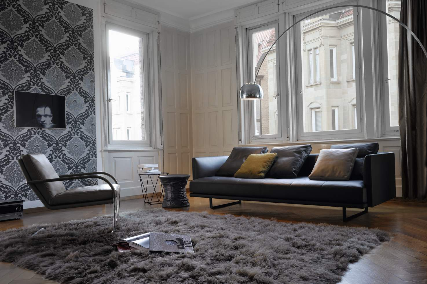 Wohnzimmer mit schwarzem Prime Time Sofa von Walter Knoll, Sessel und grauem Teppich.