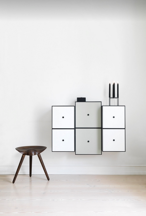 ML42 Audo Hocker aus dunklem Holz mit drei Beinen vor weißer Wand und Regalsystem.