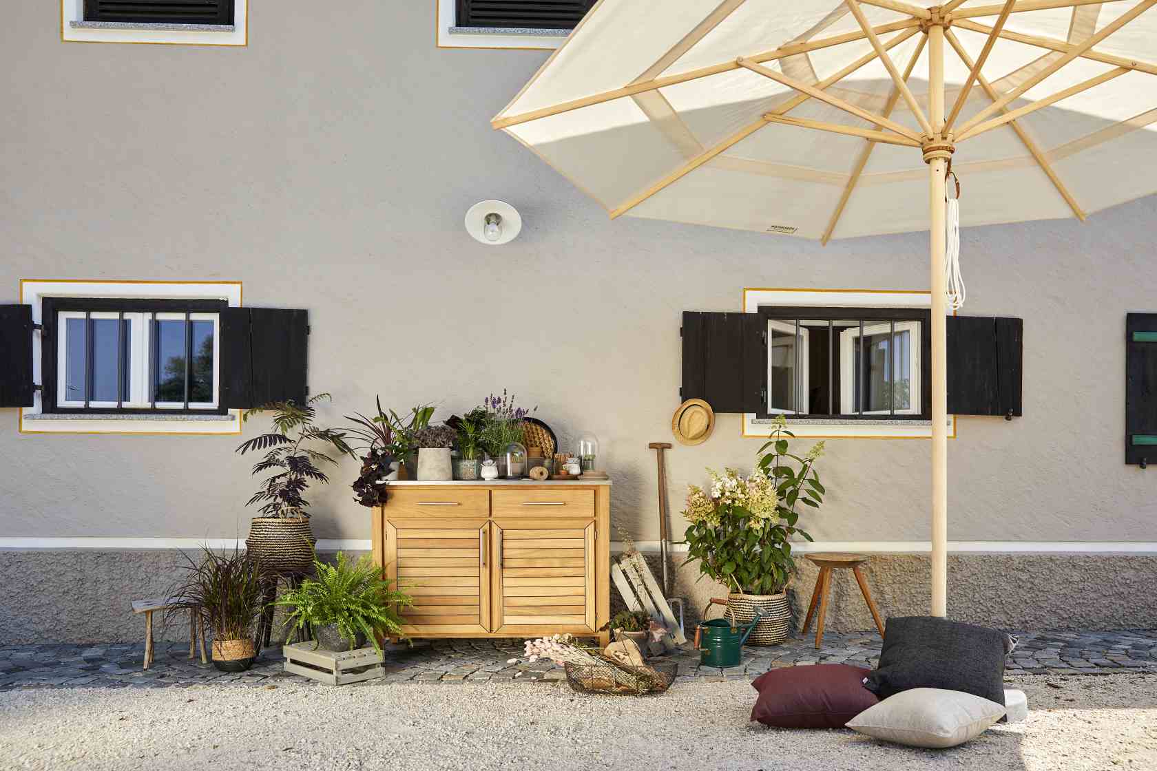 Weishäupl Klassiker Sonnenschirm aus Holz mit hellem Stoffbezug im Gartenambiente mit Pflanzen und Dekoration.