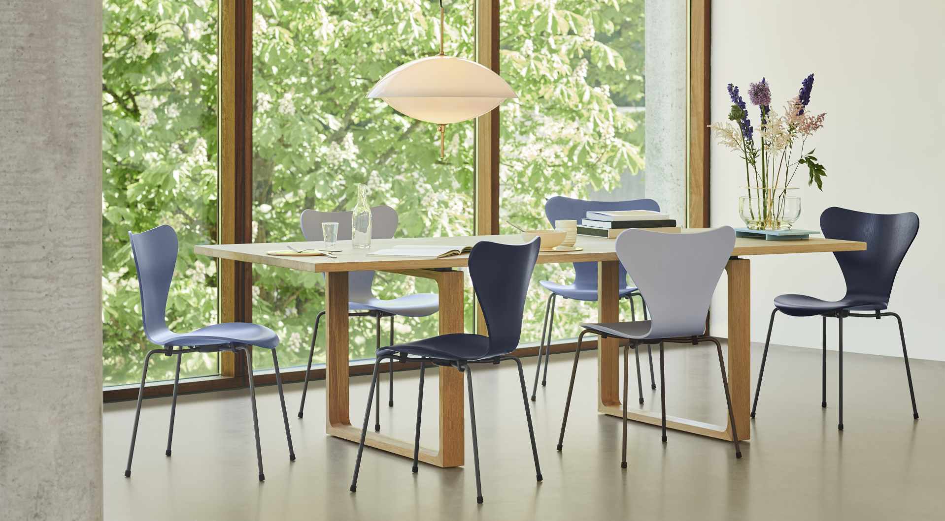 Esszimmer mit hellem Holztisch (Essay Tisch von Fritz Hansen) und blauen Stühlen vor Fenster.