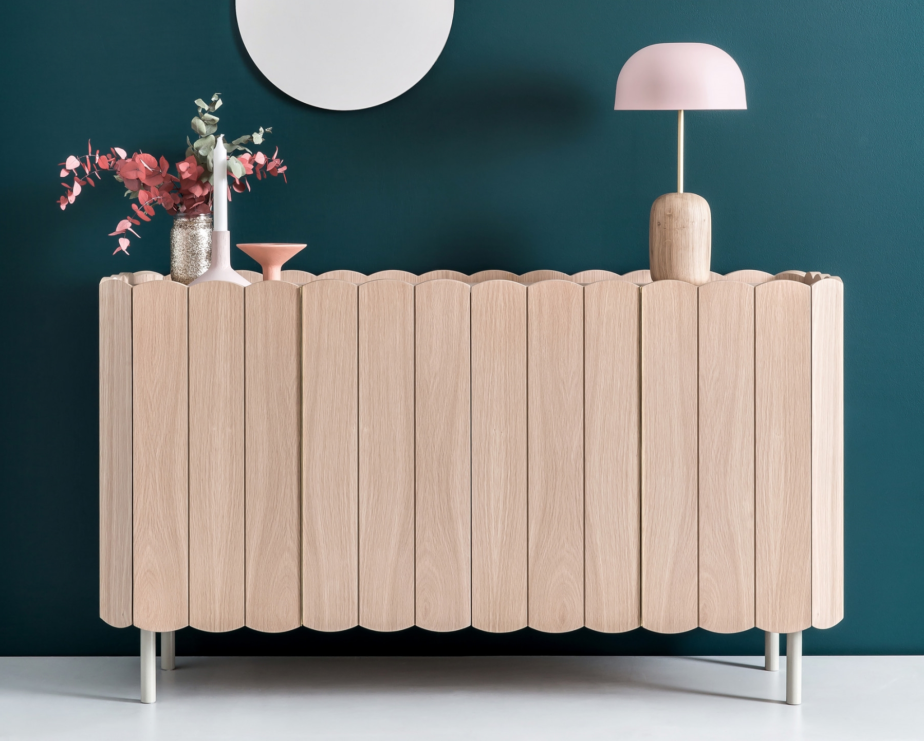 Helles Sideboard aus Eichenholz mit gewellter Kante, Lampe und Dekoration vor dunkelblauer Wand.