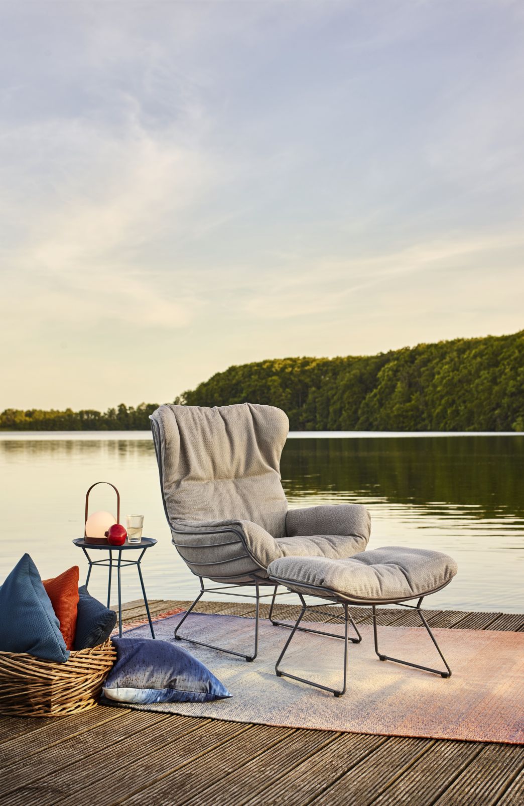 Leyasol Ottoman Outdoor von Freifrau Manufaktur auf Holzsteg am See, mit Beistelltisch und Kissen.