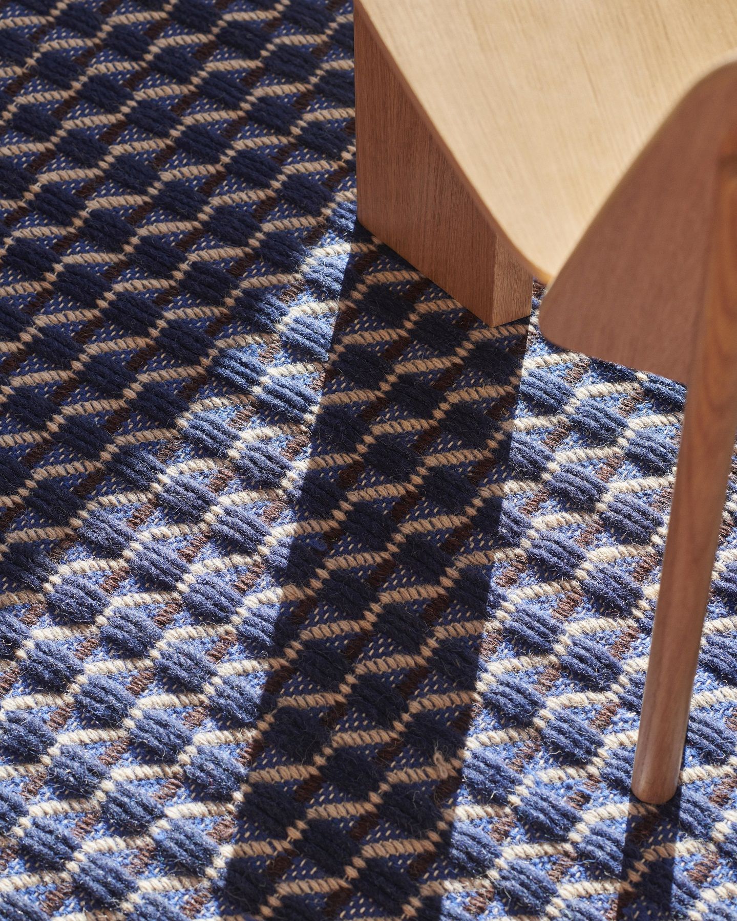 Detailaufnahme des blau-weißen Channel Rug Teppichs von Hay mit geometrischem Muster und Holzstuhlbein.