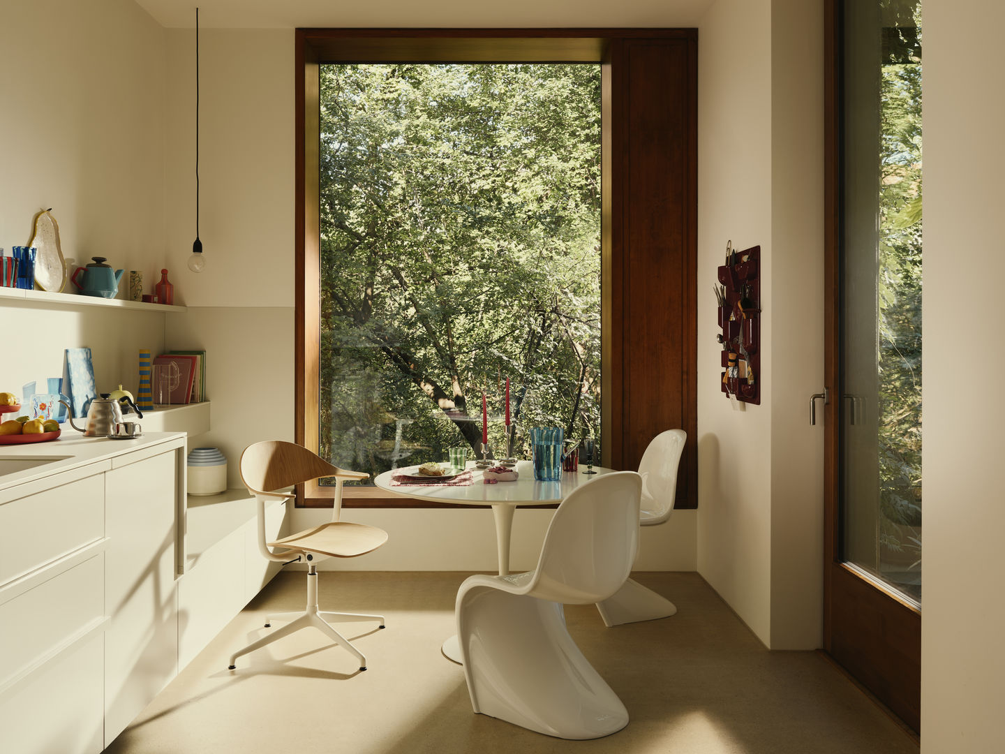 Heller Raum mit Mynt Bürodrehstuhl von Vitra aus Holz und weißen Kunststoffstühlen am runden Tisch.