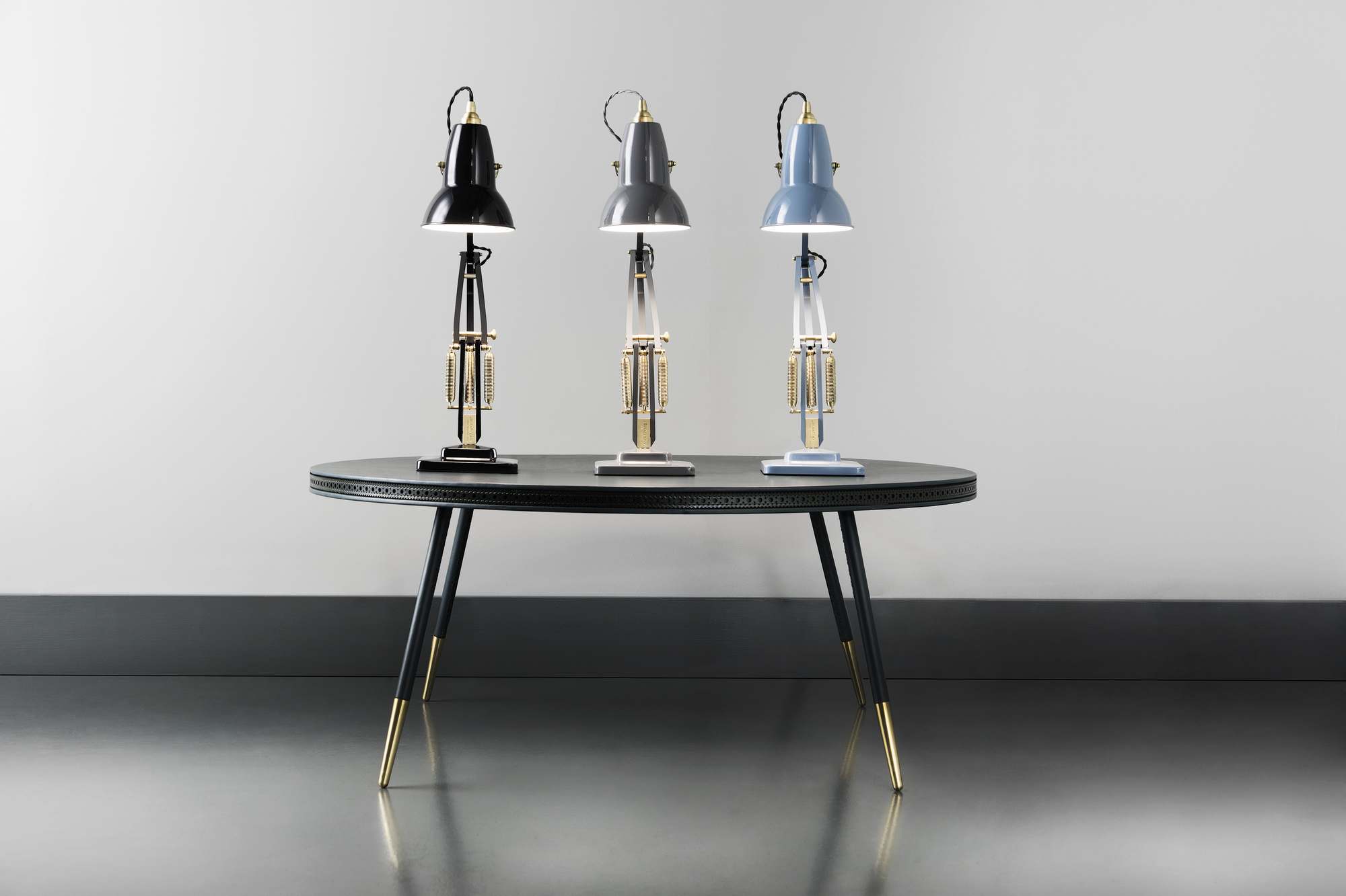 Drei Anglepoise Original 1227 Brass Tischleuchten in Schwarz, Grau und Blau auf einem Tisch.
