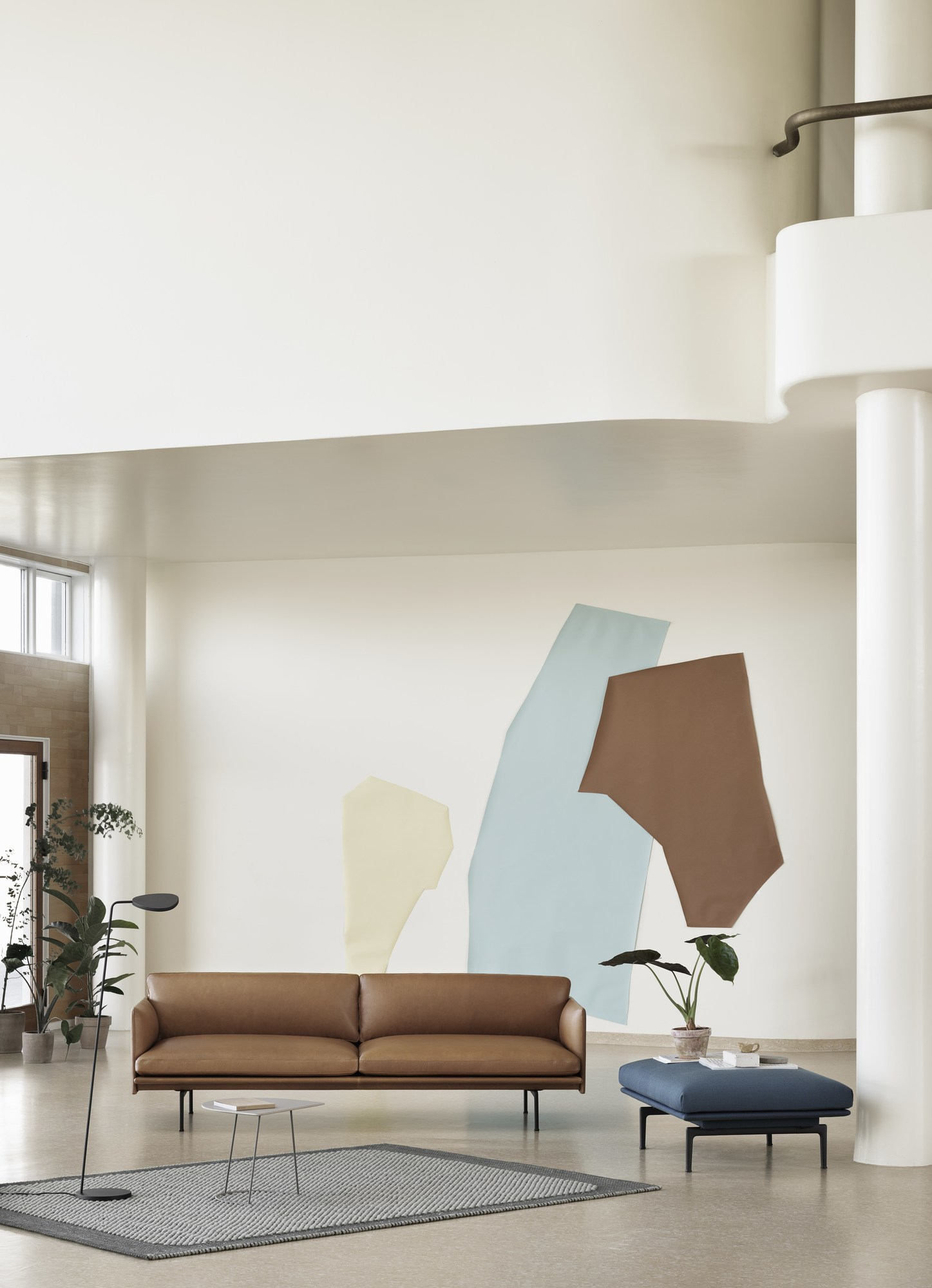 Muuto Pebble Rug Teppich in Grau unter braunem Ledersofa und blauem Hocker in hellem Raum.