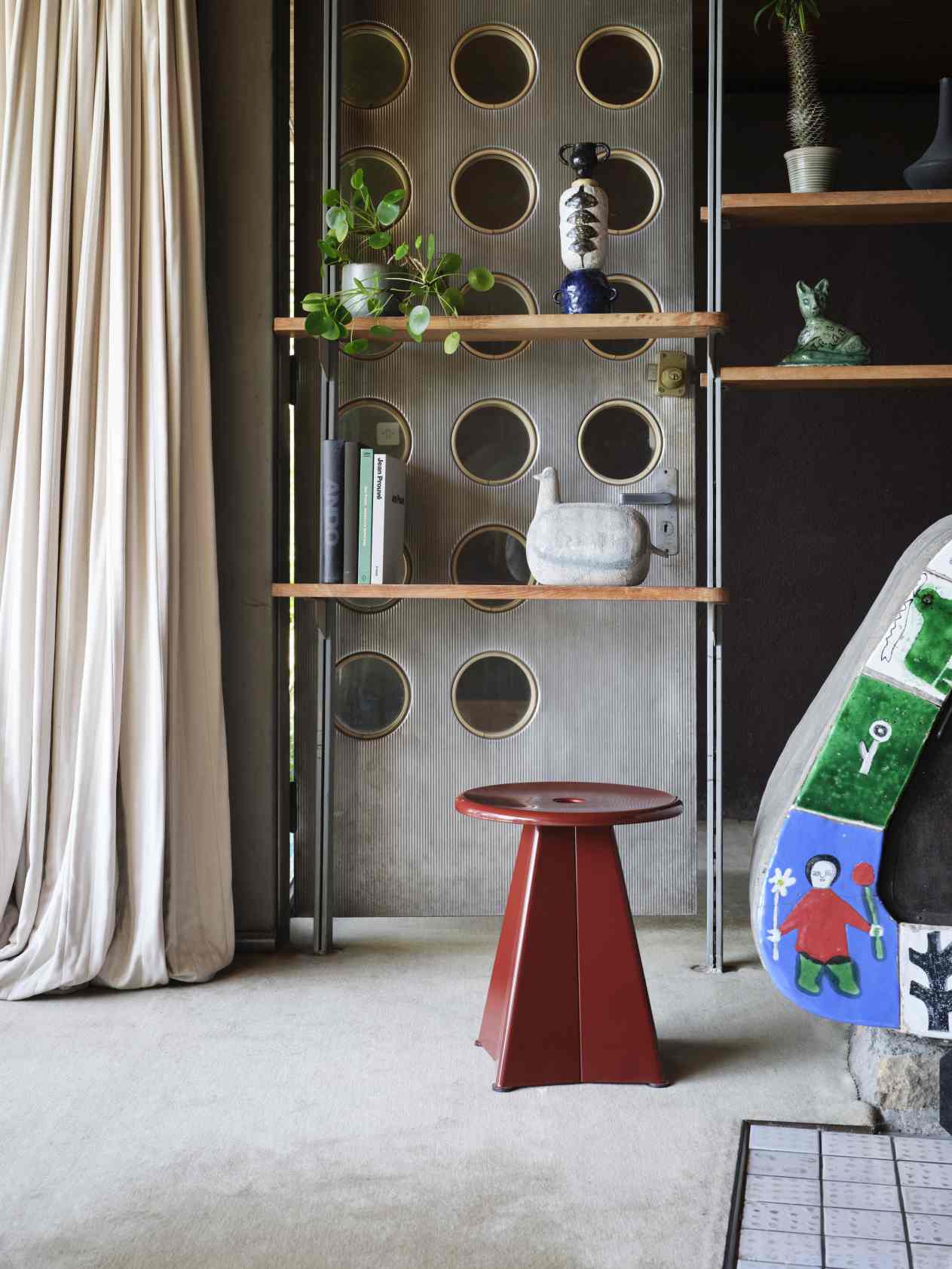 Nahaufnahme des roten Vitra Tabouret Métallique Hockers in einem stilvollen Interieur mit Regalen.