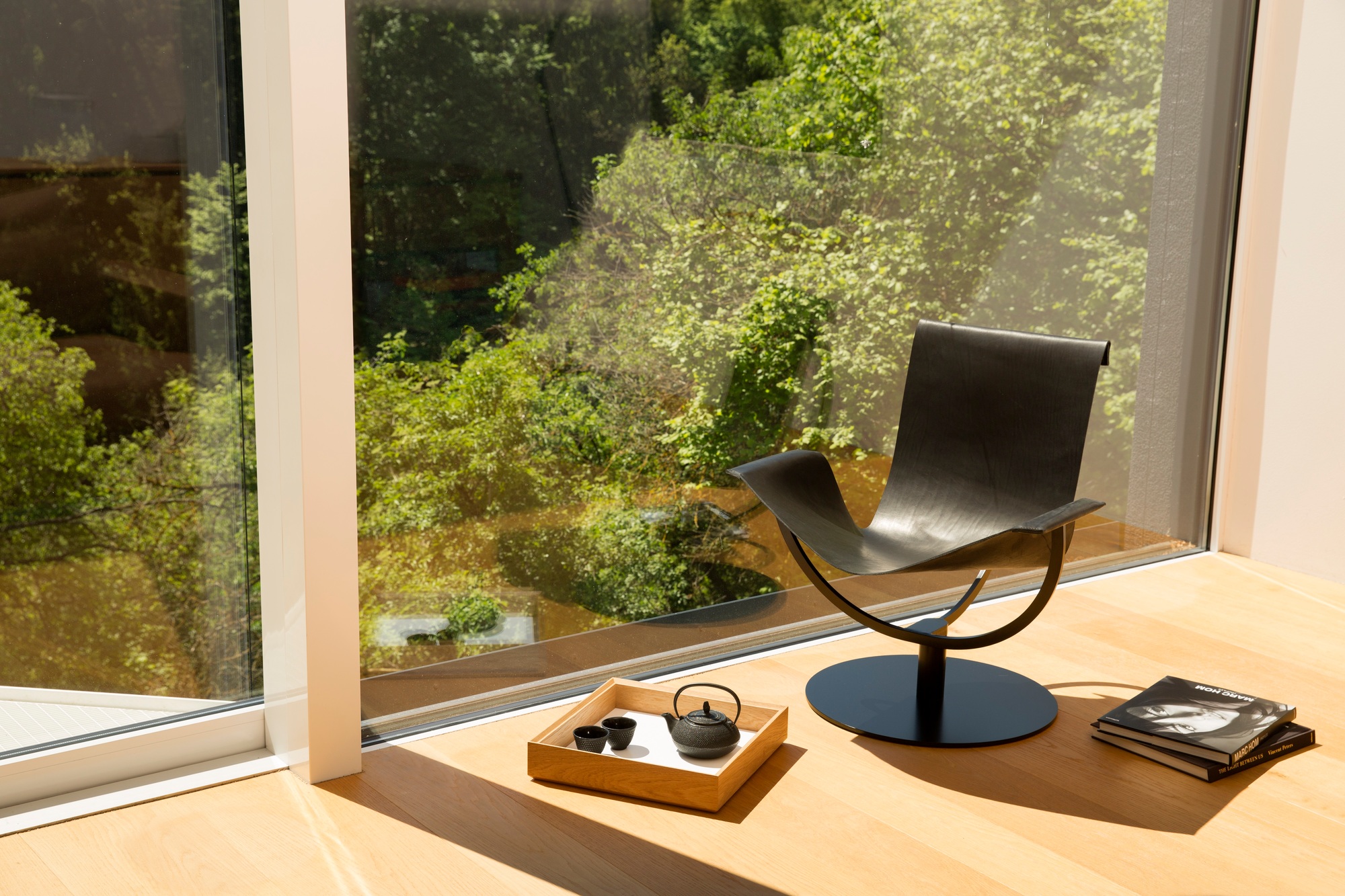 Arch Chair Sessel Favius aus schwarzem Leder vor Fenster mit Teegeschirr und Büchern.