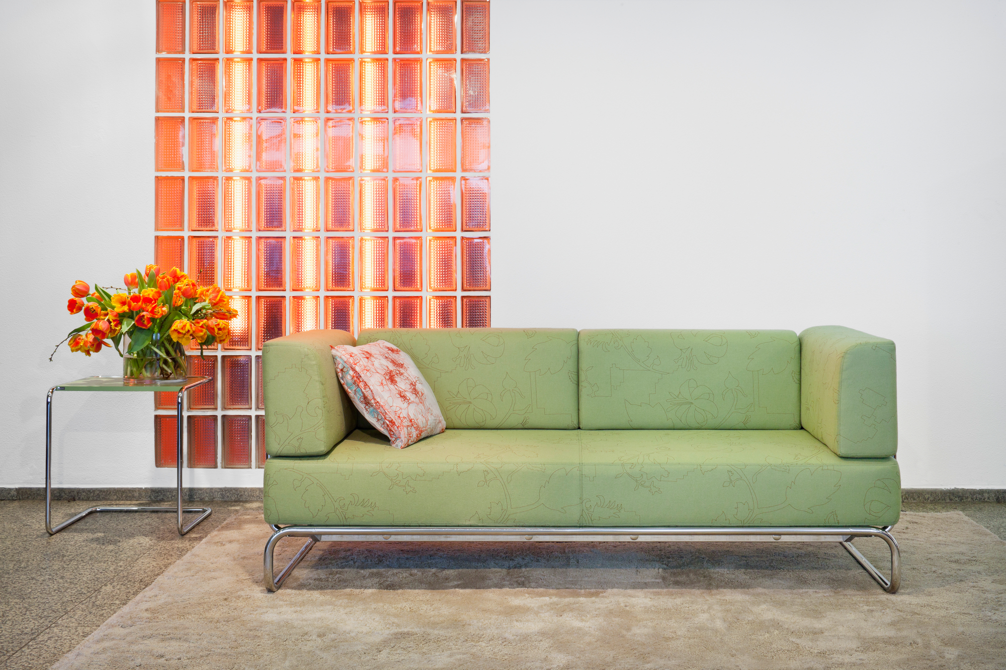 B97 a Thonet Beistelltisch aus Stahlrohr neben einem grünen Sofa und einem Blumenstrauß.