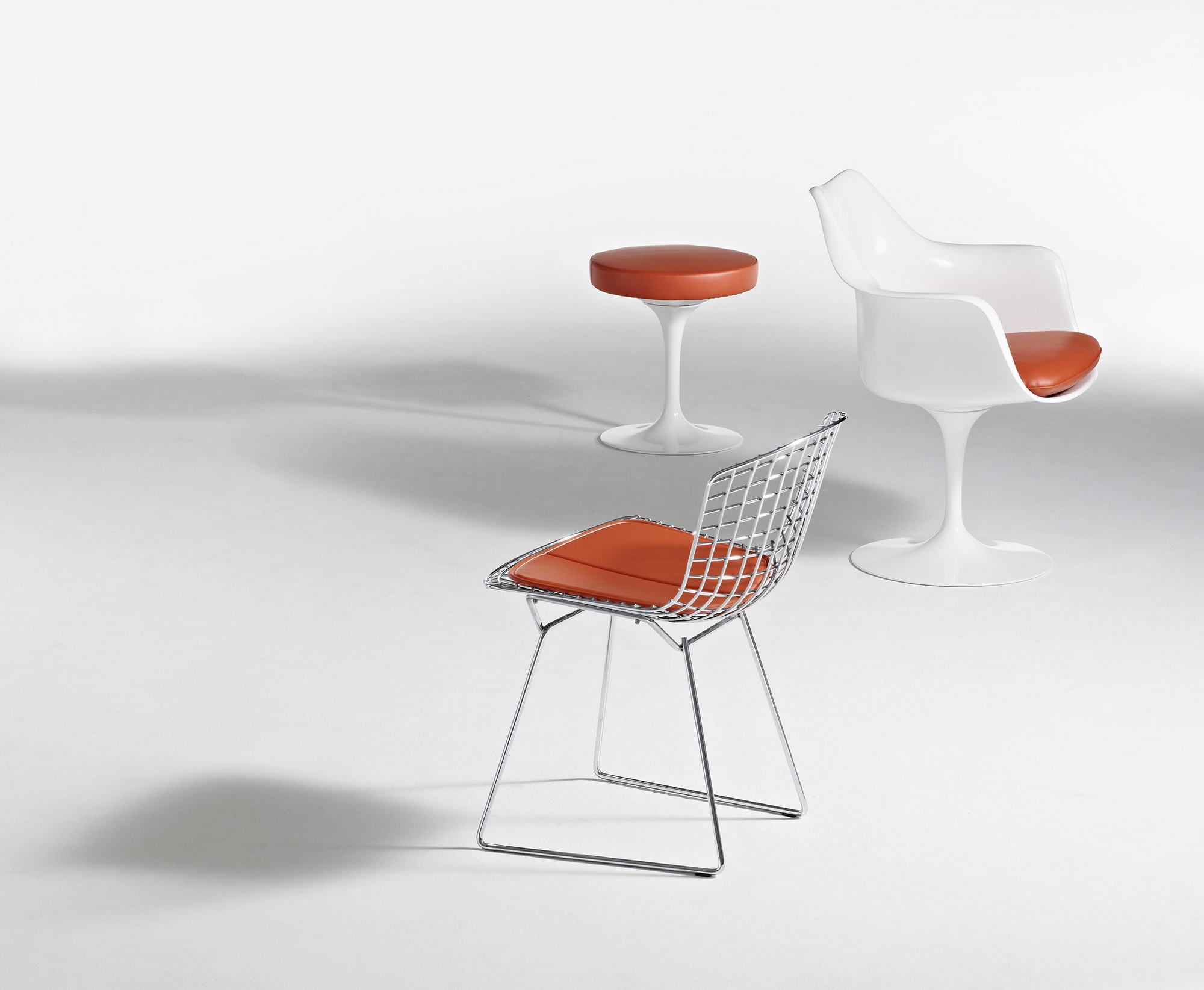 Knoll International Tulpen Armlehnenstuhl drehbar und weitere Designermöbel mit orangefarbenen Sitzkissen auf weißem Hintergrund.