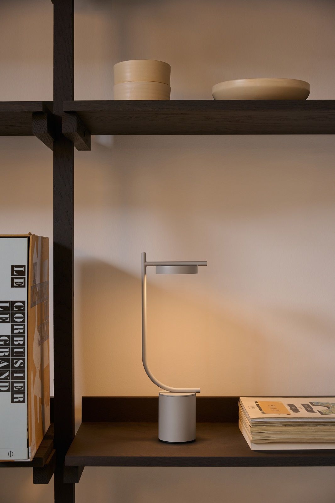 Igram Akku Tischleuchte von Grupa  auf dunklem Holzregal, modernes Design, warmes Licht.