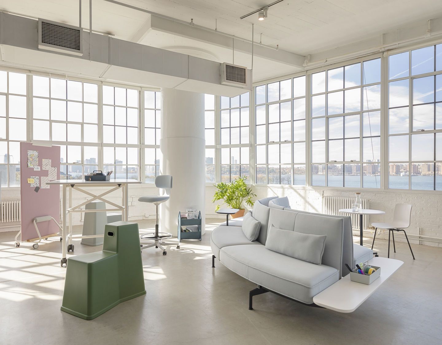 Helles Büro mit Vitra Rookie High Bürodrehstuhl, Stehtisch, Sofa und großem Fenster mit Blick auf die Stadt.
