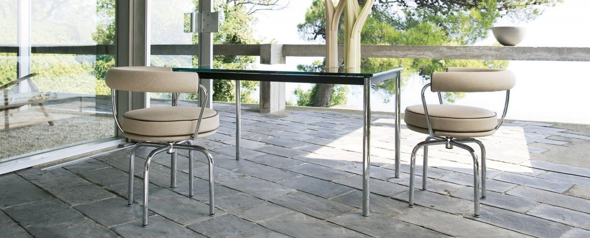 Zwei Cassina Drehsessel "7 Fauteuil Tournant" mit beigen Polstern und Chromgestell an einem Tisch.