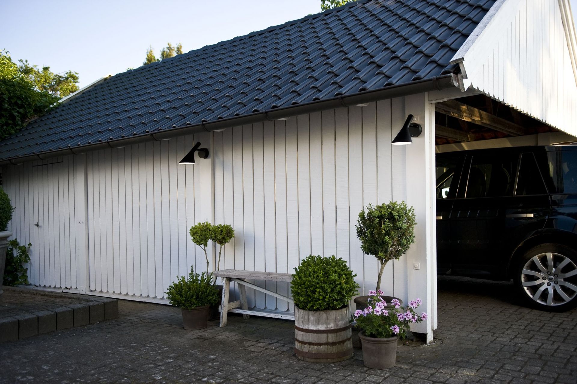 AJ 50 Wandleuchte von Louis Poulsen an weißer Holzfassade eines Hauses mit Garage und Außenbereich.