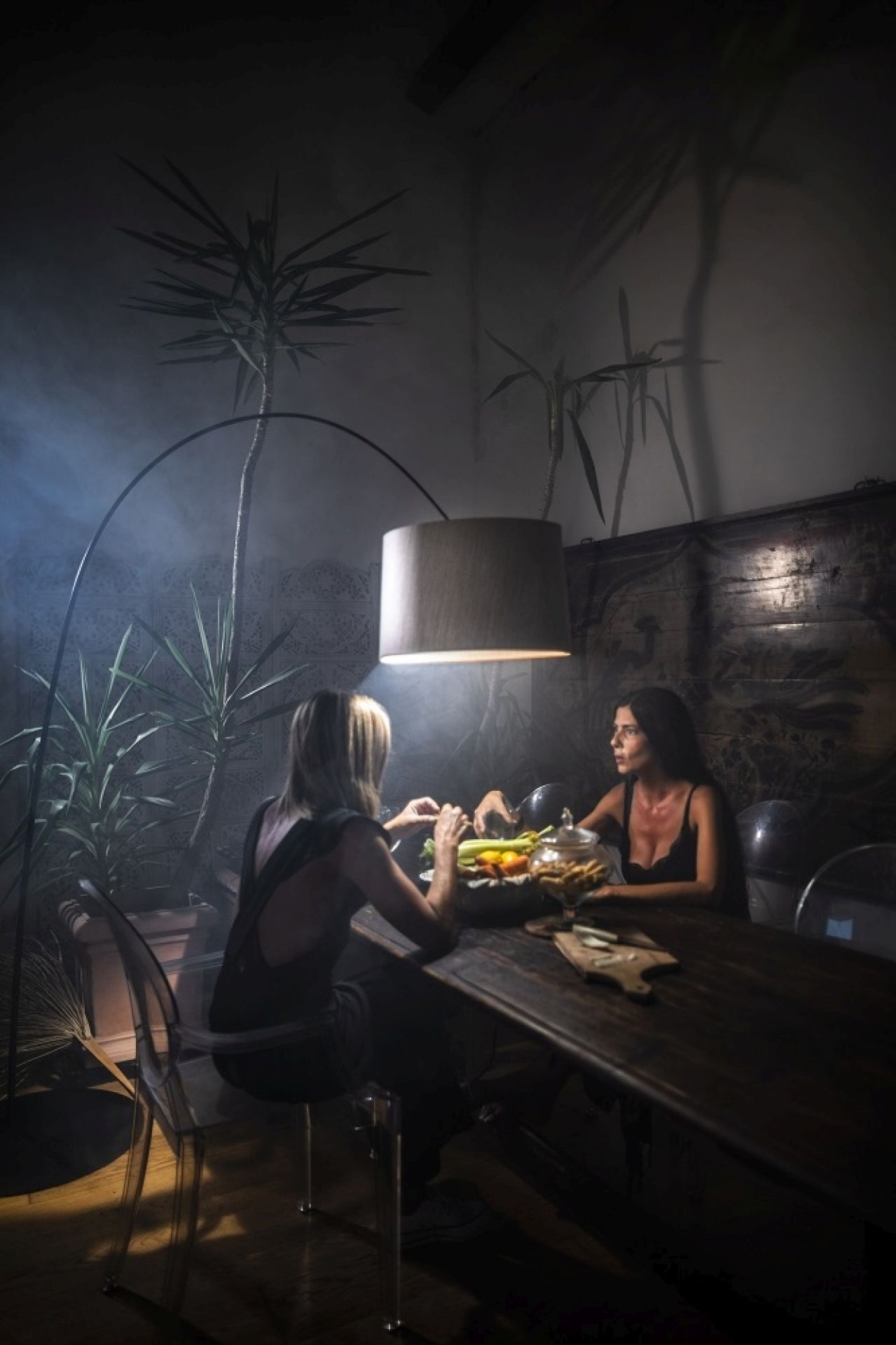 Zwei Frauen sitzen unter einer Twiggy Bogenleuchte von Foscarini an einem dunklen Holztisch.
