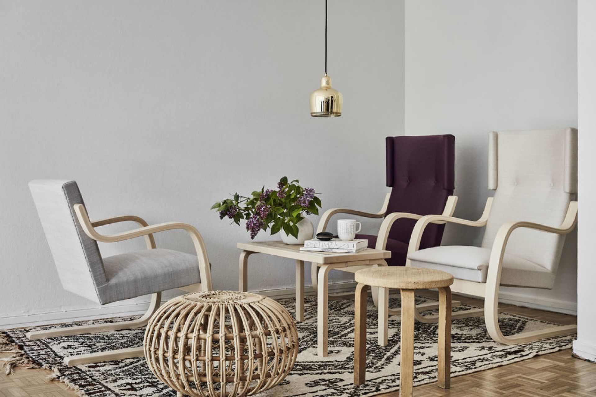 Wohnzimmer-Szene mit Artek A330S Golden Bell Pendelleuchte über einem Tisch, umgeben von Stühlen und Dekoration.