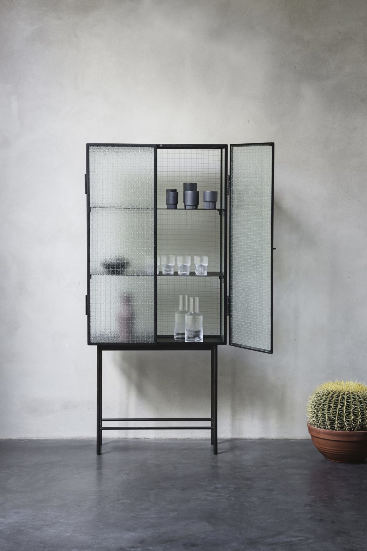 Haze Vitrine von Ferm Living aus Glas und Metall, mit Geschirr und Dekoration.