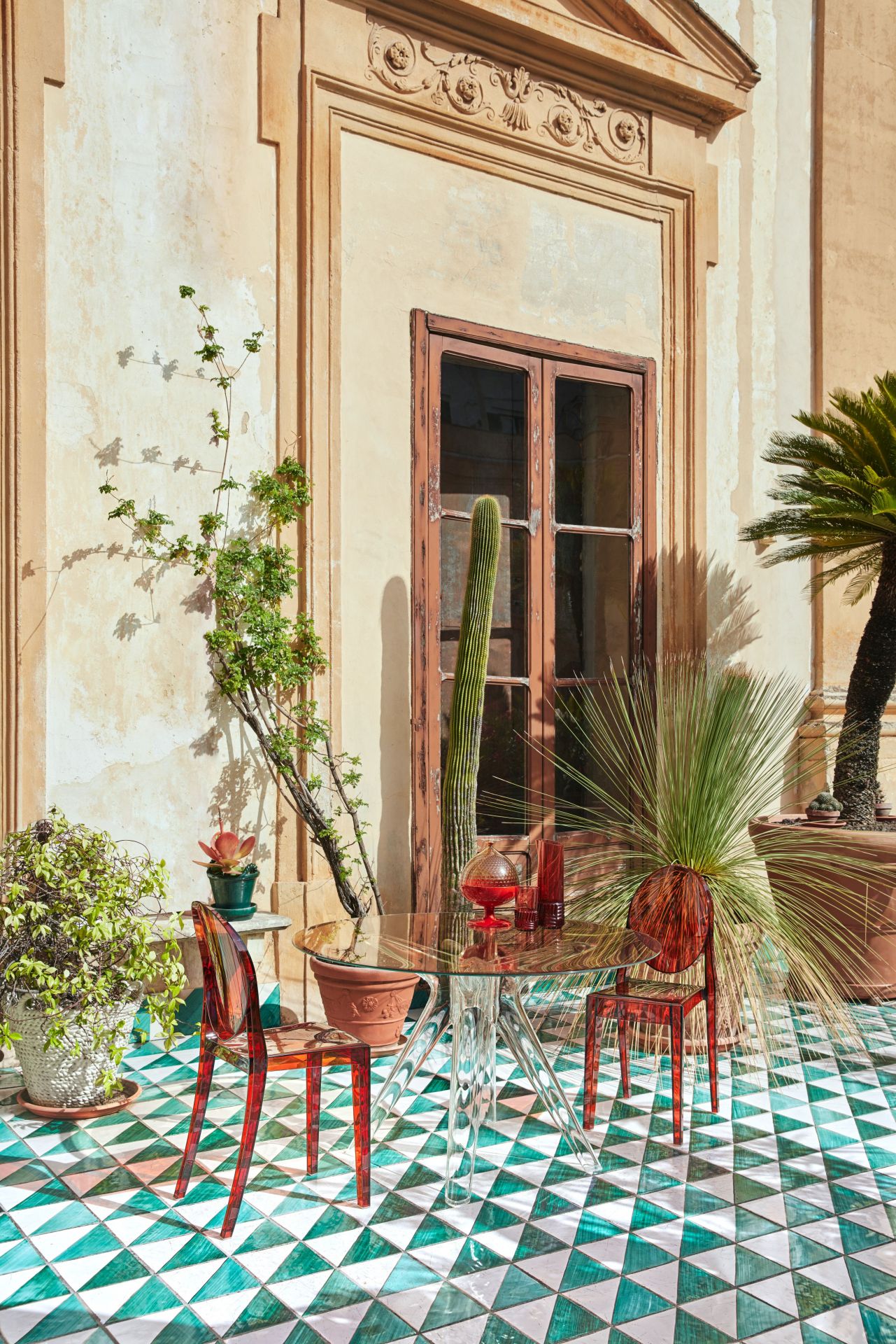 Victoria Ghost Stuhl von Kartell, glasklar, mit transparentem Tisch auf einem sonnigen, mediterranen Innenhof.