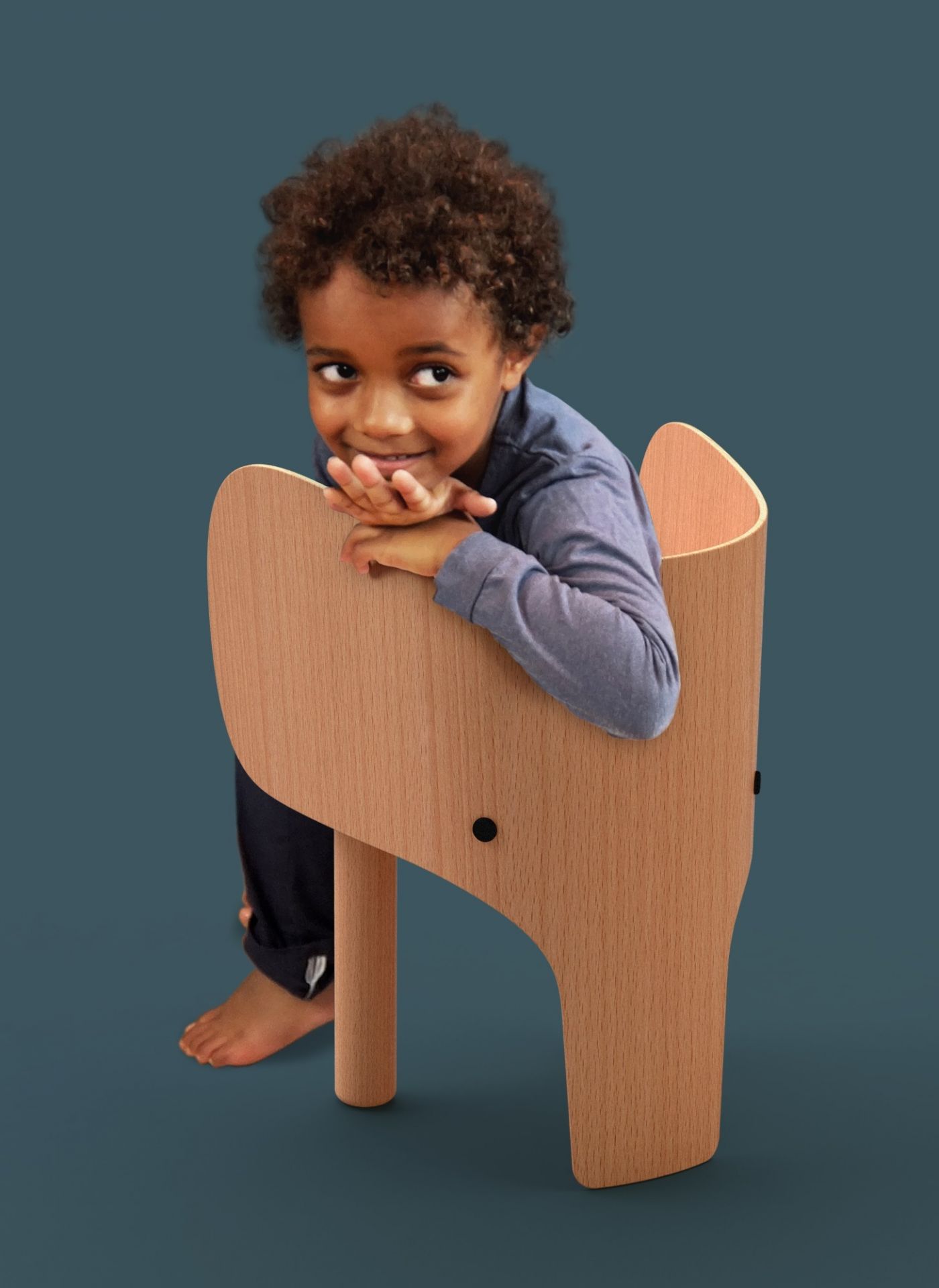 Junge lehnt lächelnd im hellen Holzstuhl in Elefantenform. Kinderstuhl, Designstuhl, EO.