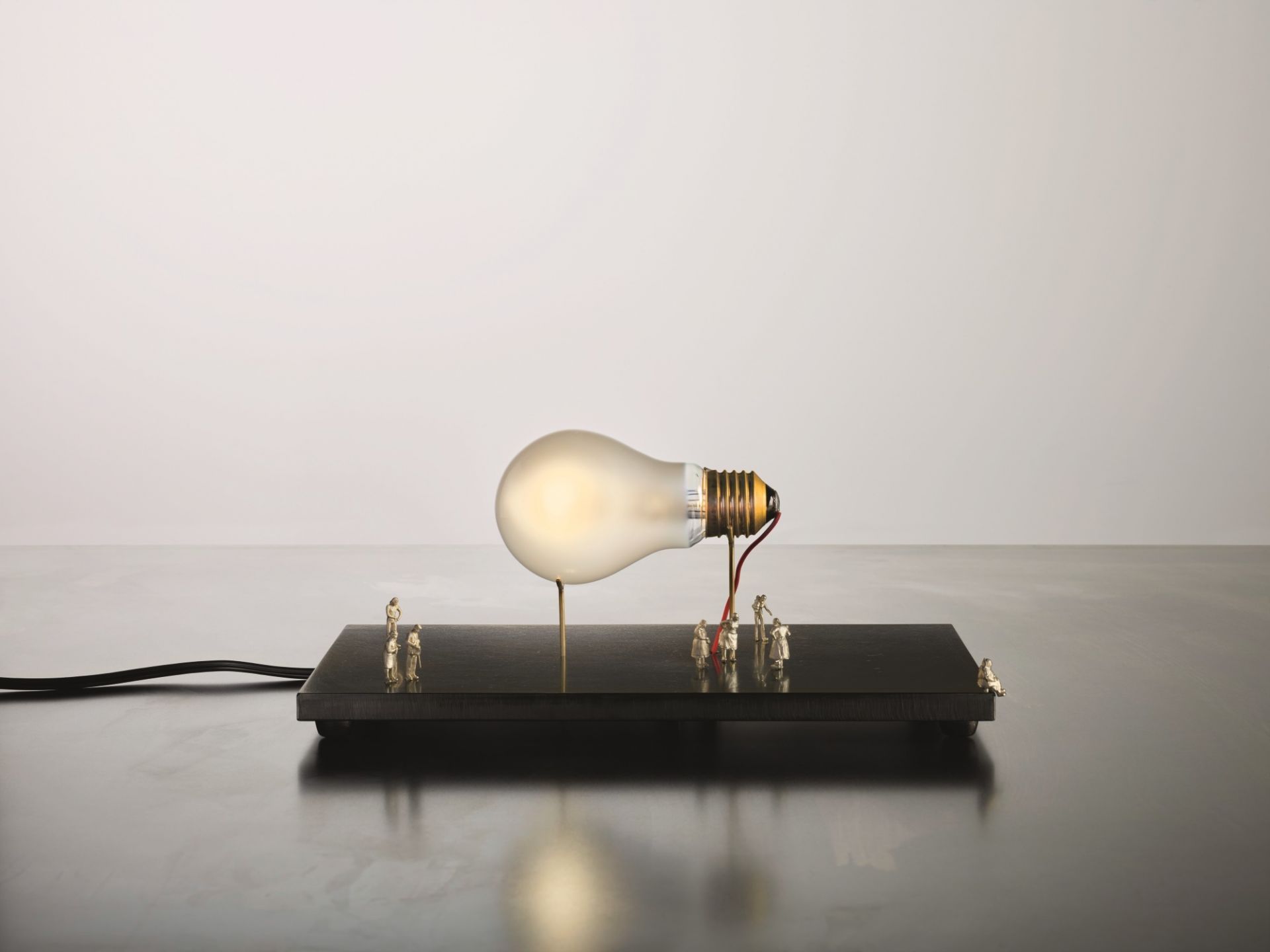 I Ricchi Poveri Tischleuchte: Glühbirne auf Sockel mit kleinen Figuren. Designlampe von Ingo Maurer.