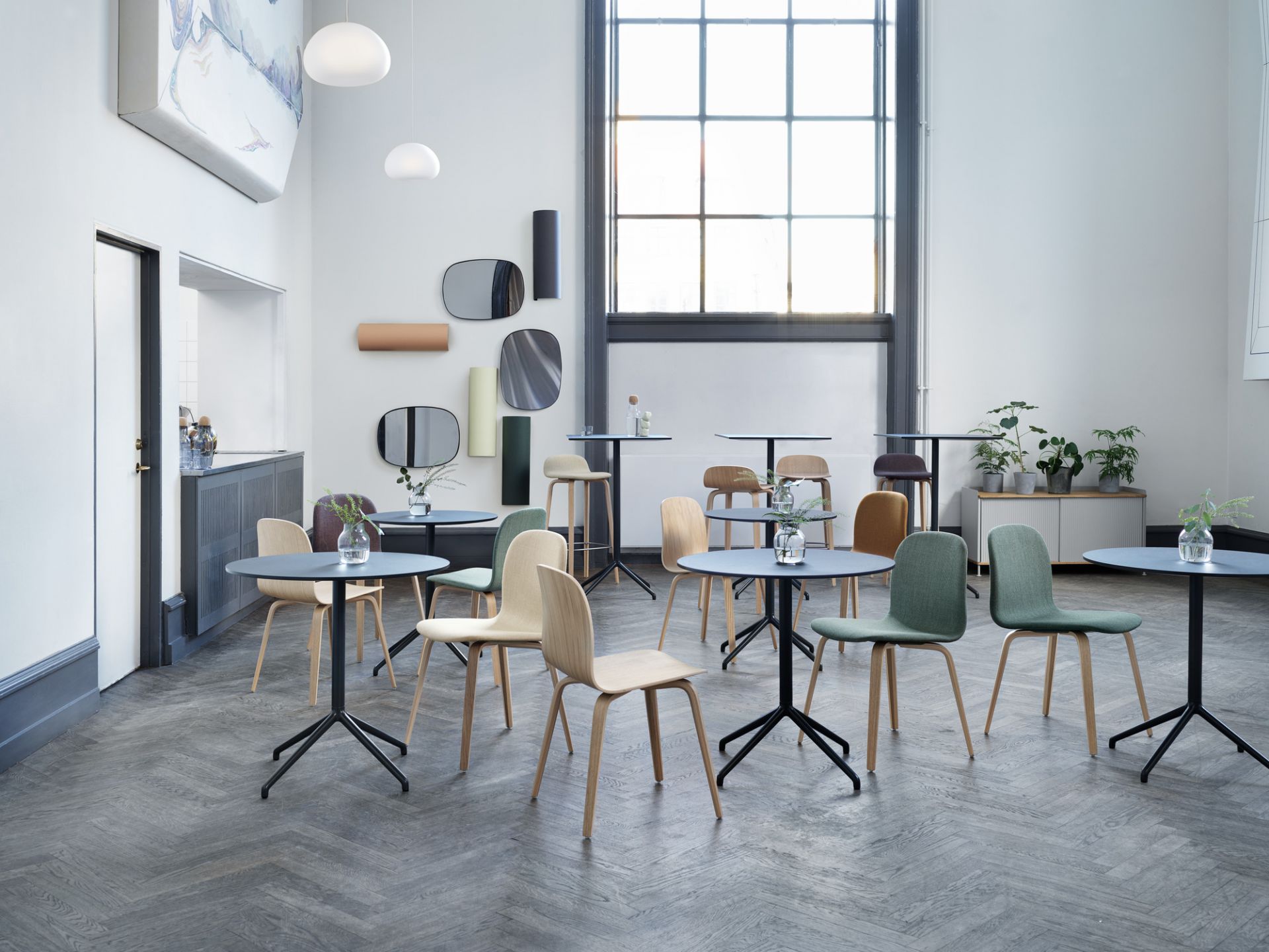 Innenaufnahme eines Cafés mit mehreren Muuto Still Cafe Tischen und Stühlen auf einem grauen Fischgrätenboden.
