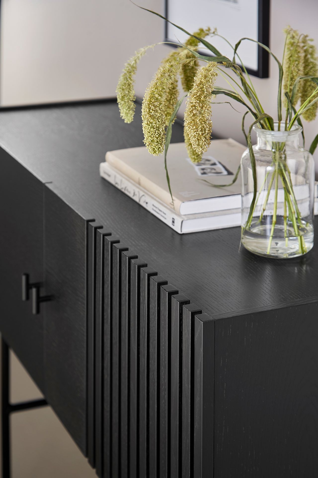 Detailaufnahme des schwarzen Array Sideboards von Woud (120cm) mit geriffelter Front, Büchern und Blumenvase.