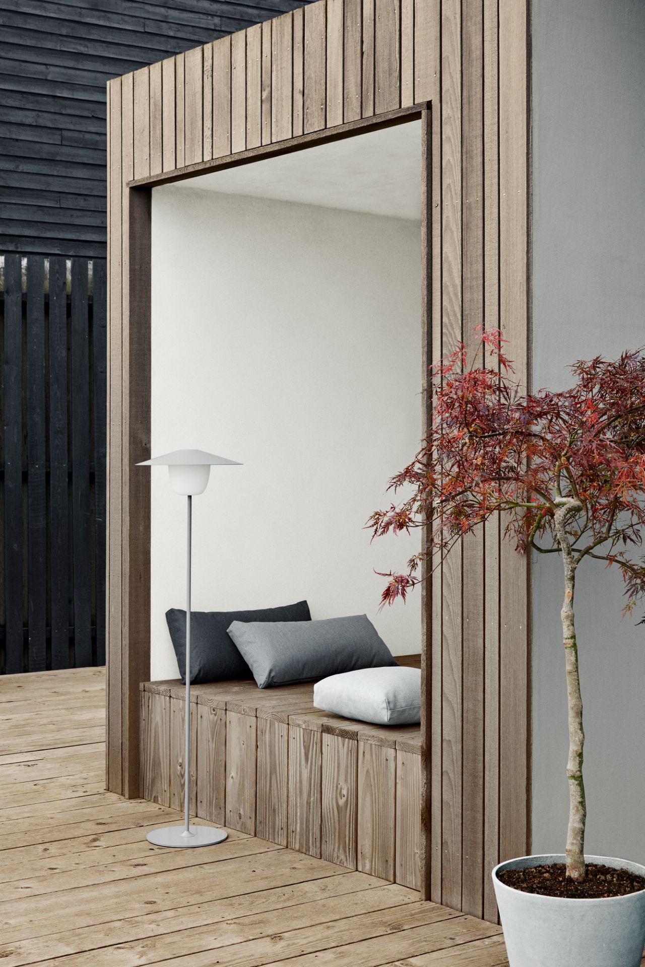 Drei STAY Kissen Outdoor von Blomus auf einer Holzbank, mit Lampe und Baum.