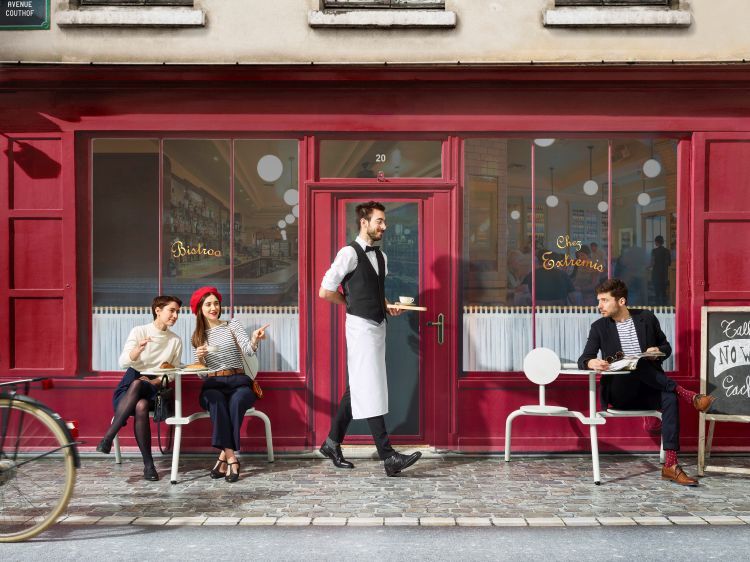 Extremis Bistroo Stuhl-Tisch-Kombination für den Außenbereich vor rotem Bistro mit Gästen und Kellner. Outdoor Möbel.