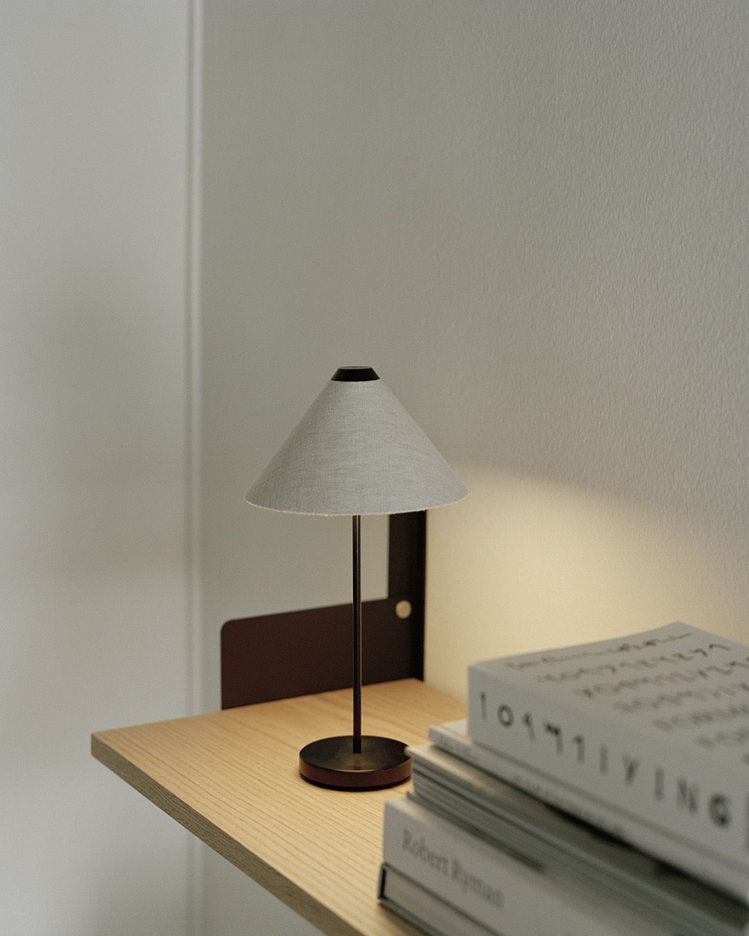 New Works Brolly Tischleuchte mit grauem Stoffschirm auf einem Holztisch neben Büchern.