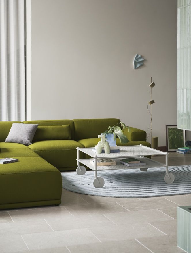 Muuto Flow Couchtisch auf Rollen, weiß, mit Pflanzen und Büchern dekoriert, vor grünem Sofa.